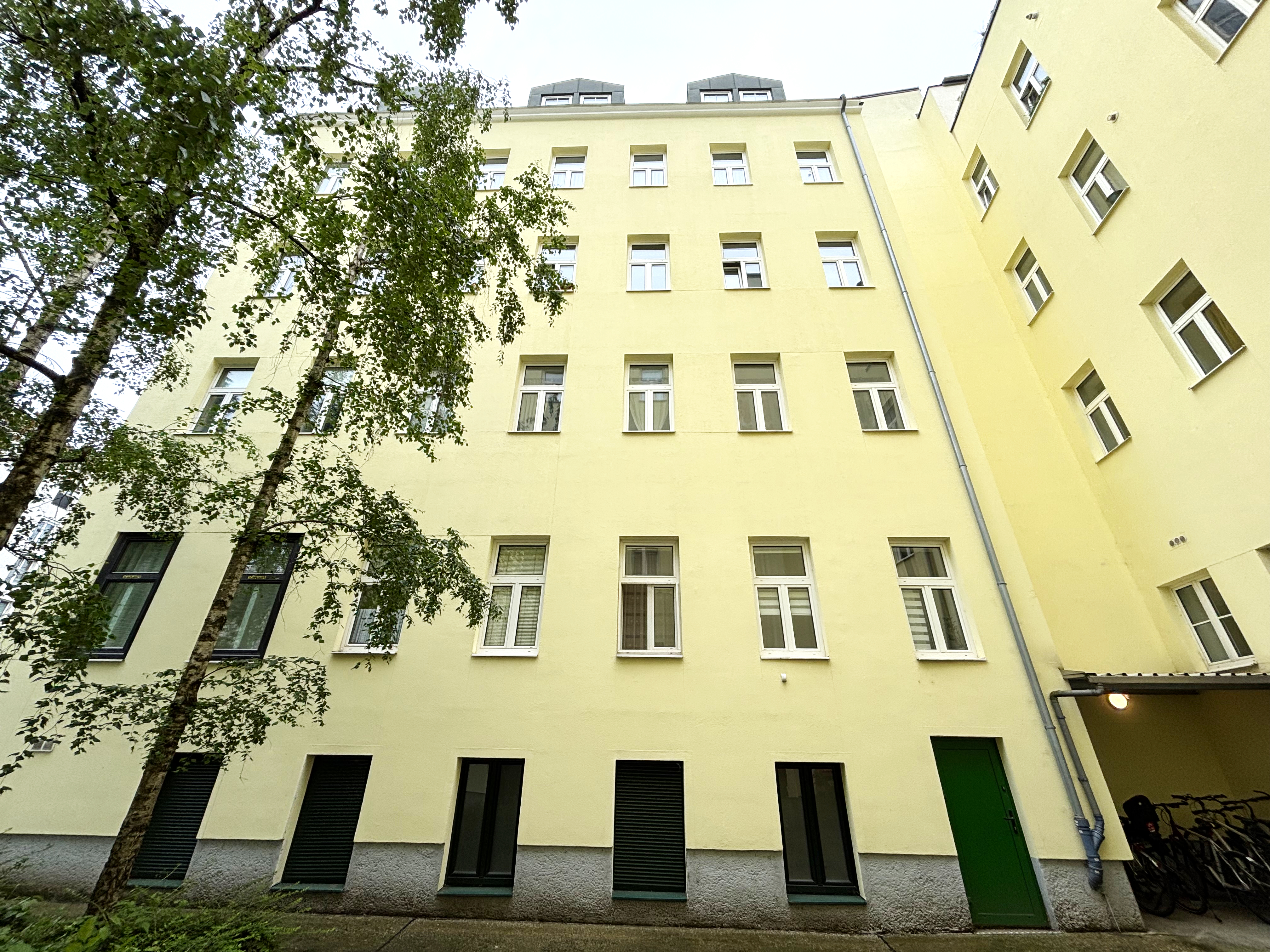 saniertes Altbauhaus, gelbe Fassade, weiße Fenster, Innenhofblick , links 3 Laubbäume, Wohnung im 12. Bezirk Wien