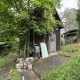 Baugrundstück im 17. Bezirk von Wien, kleines Holzhaus, dunkelbraun, umsäumt von einer betonierten Terrasse, grüne Wiese und Bäume