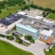 großes Druckhaus in St. Pölten, großer moderner Gebäudekomplex, mit Parkplätzen, Zufahrtstraße im Vordergrund, Wiesen und Felder im Hintergrund