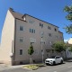 Wohnung in Wr. Neustadt, Haus mit beiger Fassade, Fenster weiß, Straße im Vordergrund, weißer Mercedes parkt davor, blauer Himmel