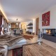 sehr schöne, luxuriöse Wohnung mit alpinem Charme in Kitzbühel, großzügiger Wohn- und Essraum, mit Holzboden, Sofa mit Couchtisch und offener Kamin im Vordergrund, dahinter schöner Essbereich