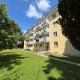 13. Bezirk von Wien, Wohnhaus mit gelber Fassade, Hauseingang, Balkone, weiße Fenster, Wiese im Vordergrund
