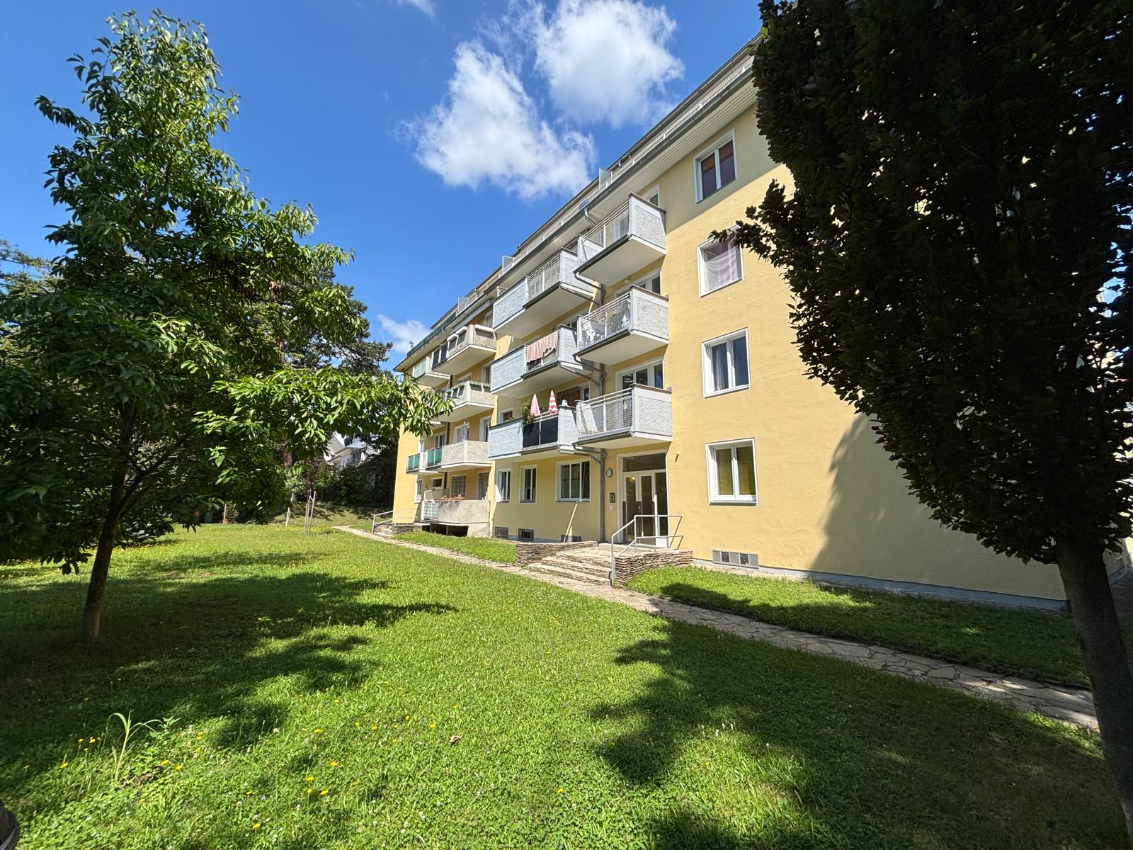 13. Bezirk von Wien, Wohnhaus mit gelber Fassade, Hauseingang, Balkone, weiße Fenster, Wiese im Vordergrund