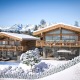 Visualisierung von zwei Einfamilienhäusern im Chale-Charakter in Kitzbühel, Dächer, Berge im Hintergrund und Wiese davor mit Schnee bedeckt, blauer Himmel