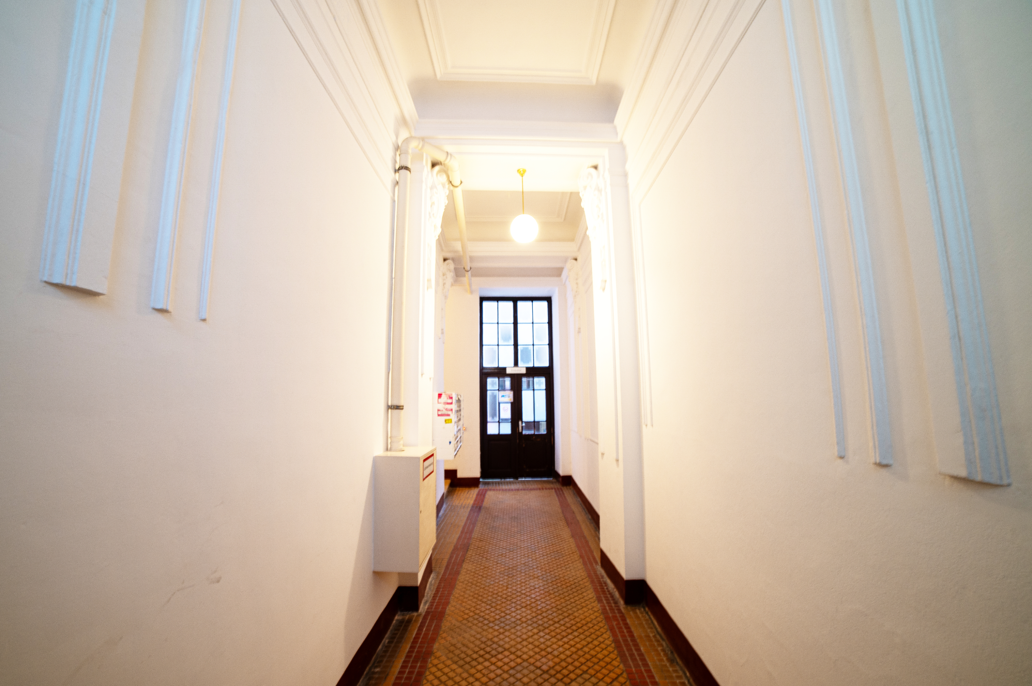 schöner Eingangsbereich ins Stiegenhaus eines sanierten Altbaus, Stuckdecken, weiße Wände, gekachelter Boden, 5. Bezirk in Wien