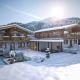 Neubauprojekt in St. Johann in Tirol, 2 exklusive Chalets - Fassade Oberstock mit Holzfenster und Holzbalkon, Holzdachgiebel, Erdgeschosse in Steinmaueroptik, mit Pool und schönem Außenbereich, verschneite Winterlandschaft