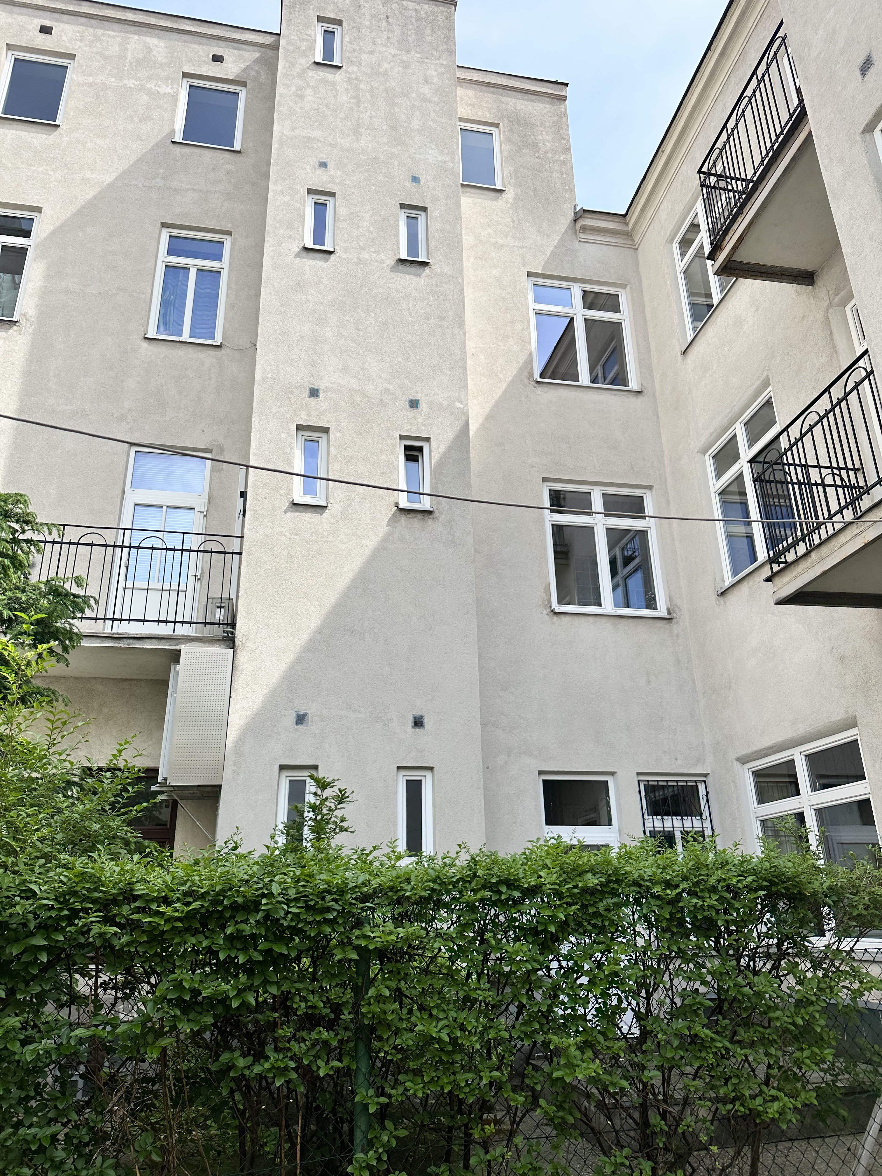 Innenhofansicht eines Zinshauses im 21. Bezirk von Wien, Fassade grau, Fenster weiß, grüne Hecke davor
