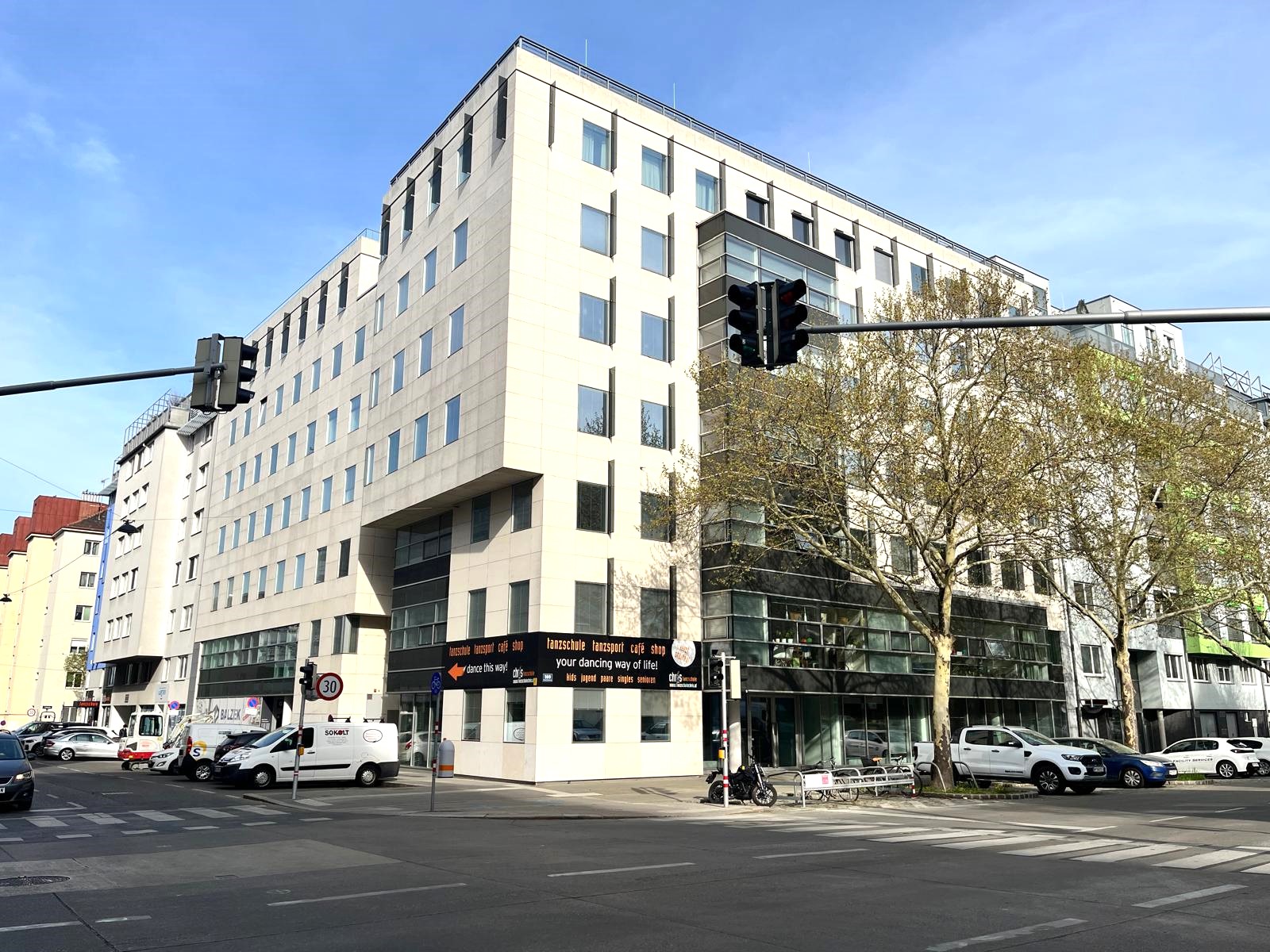 Außenansicht eines mehrstöckigen modernen Gebäudes mit einem im Erdgeschoss befindlichen Geschäftslokals/Büro, Eckgebäude an einer ampelgeregelten Kreuzung, Fassade hell, 2. Bezirk Wiens