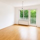 unmöbliertes Wohnzimmer einer Eigentumswohnung im 13. Bezirk Wiens, Parkettboden, weiße Wände, Fenster und Balkontür weiß, Blick ins Grüne