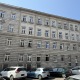 Blick auf ein Eckzinshaus im 14. Bezirk von Wien, blauer Himmel, graue Fassade, weiße Fenster
