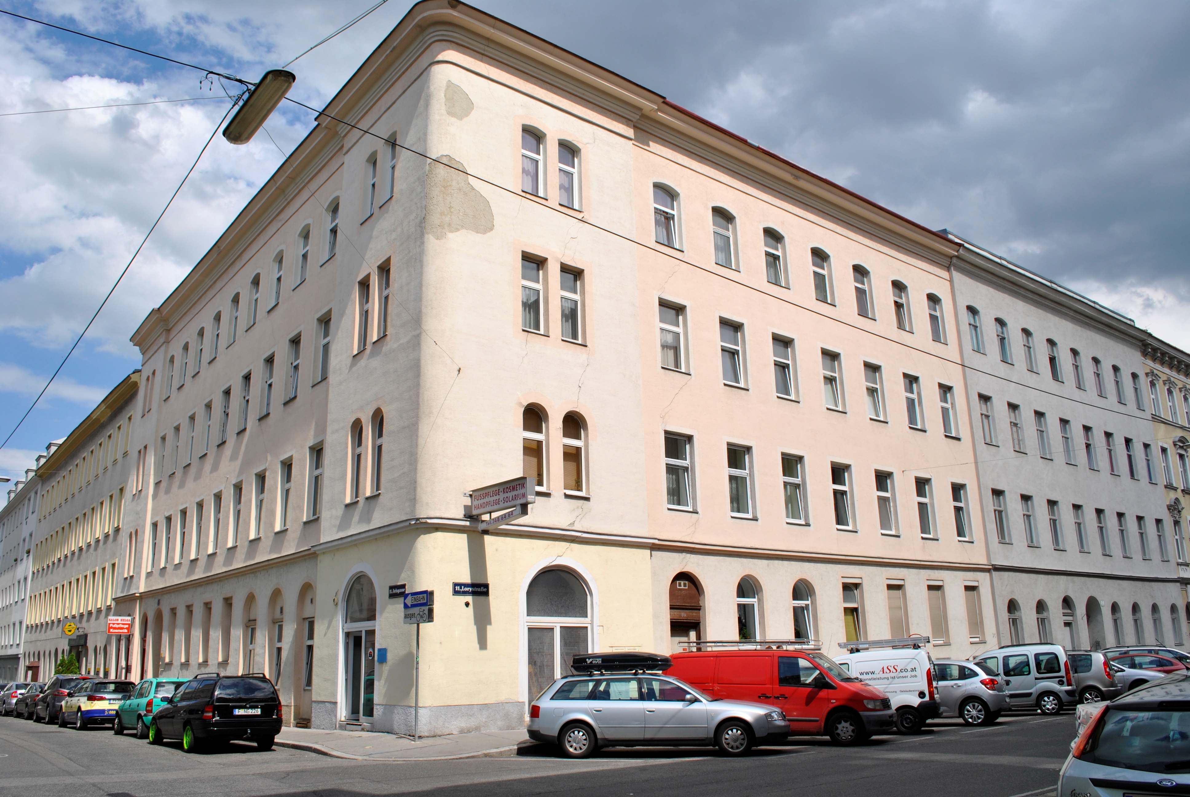 Außenansicht eines mehrstöckigen Wohnhauses im 11. Bezirk Wiens, Eckhaus, weiße Fenster, helle Fassade, parkende Autos davor
