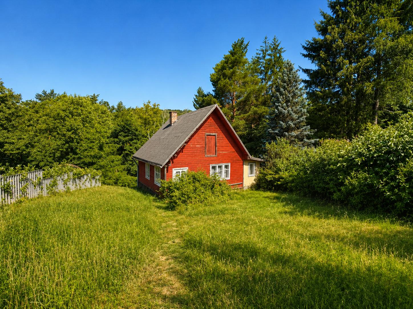 Baugrundstück im 14. Bezirk von Wien, grüne Wiese, dahinter Bäume, kleines rotes Holzhaus im Hintergrund