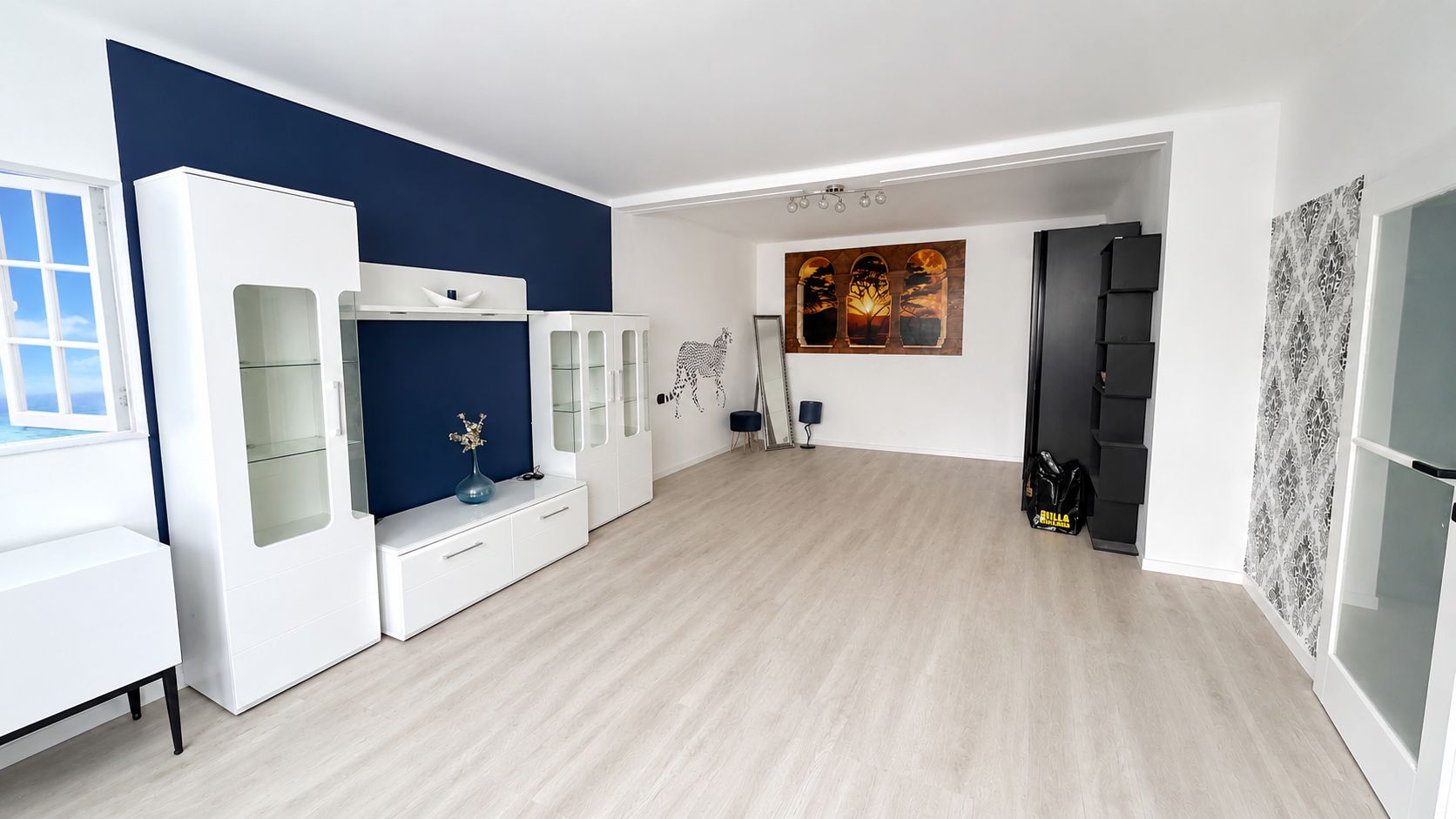 großer Wohnraum, mit weißen Möbeln, eine Wand in dunkelblau, Decke weiß, heller Boden